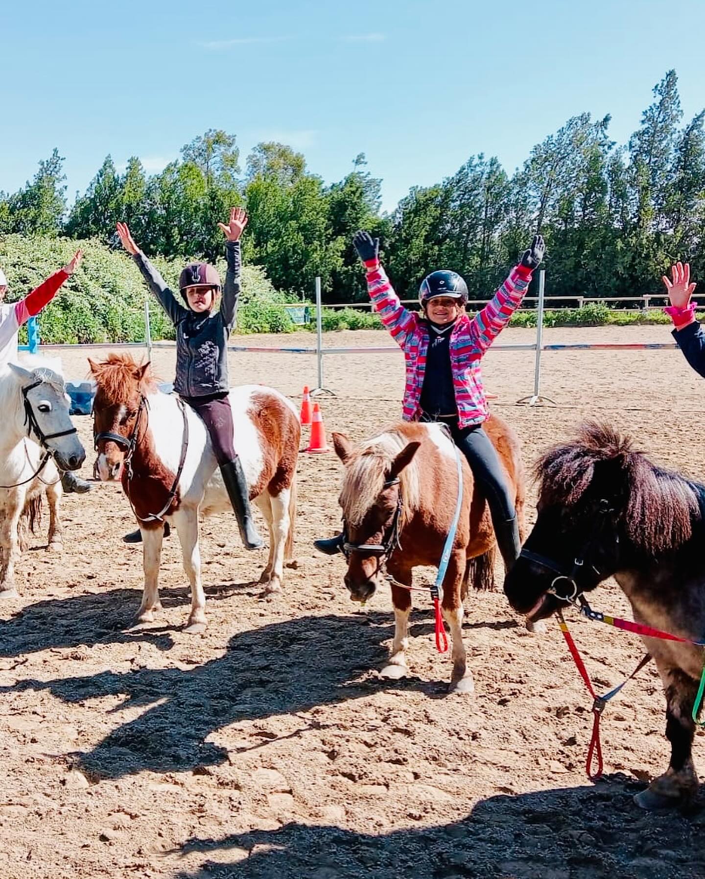Enfants à poney, bras levés, pendant un stage de Pâques