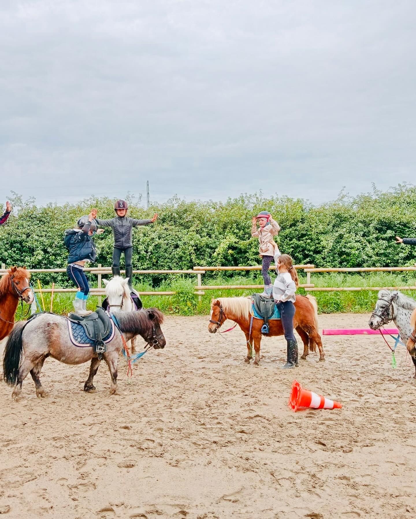 Children standing on the ponies' backs, arms outstretched, during a vaulting session in the arena